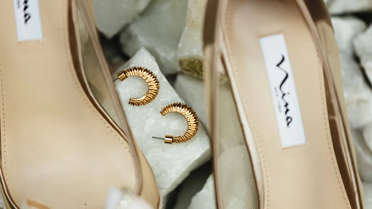 Talons beige élégants et boucles d'oreilles créoles dorées texturées sur une surface en marbre.