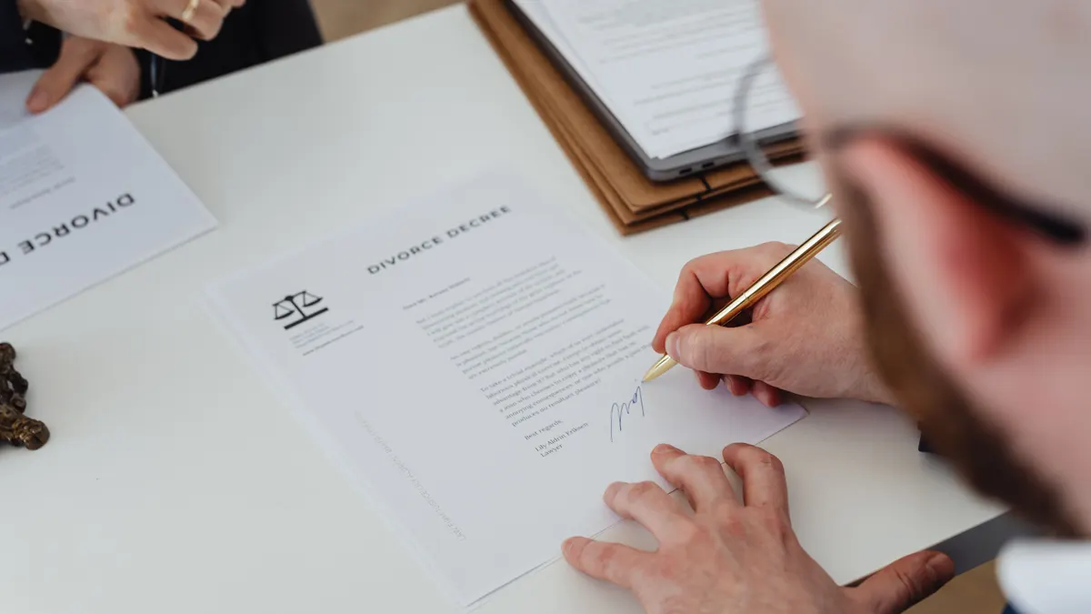 Gros plan d'une personne signant un décret de divorce sur un bureau.